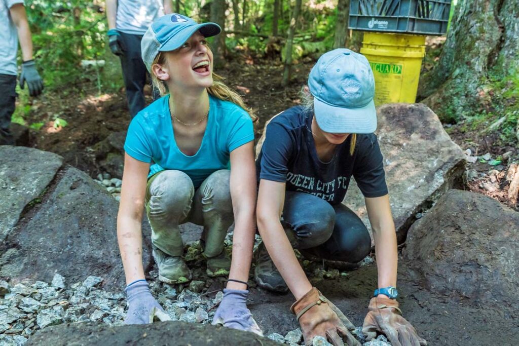 teen girls in gloves place gravel on a trail