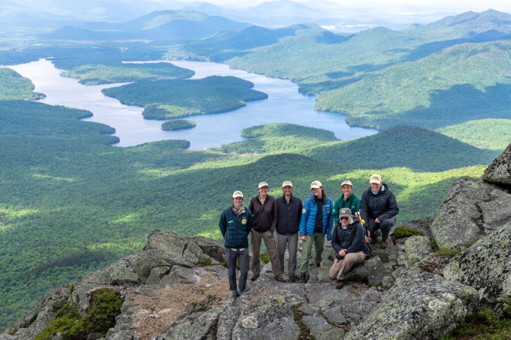 A group of people pose on a mountain with a lake in the background.