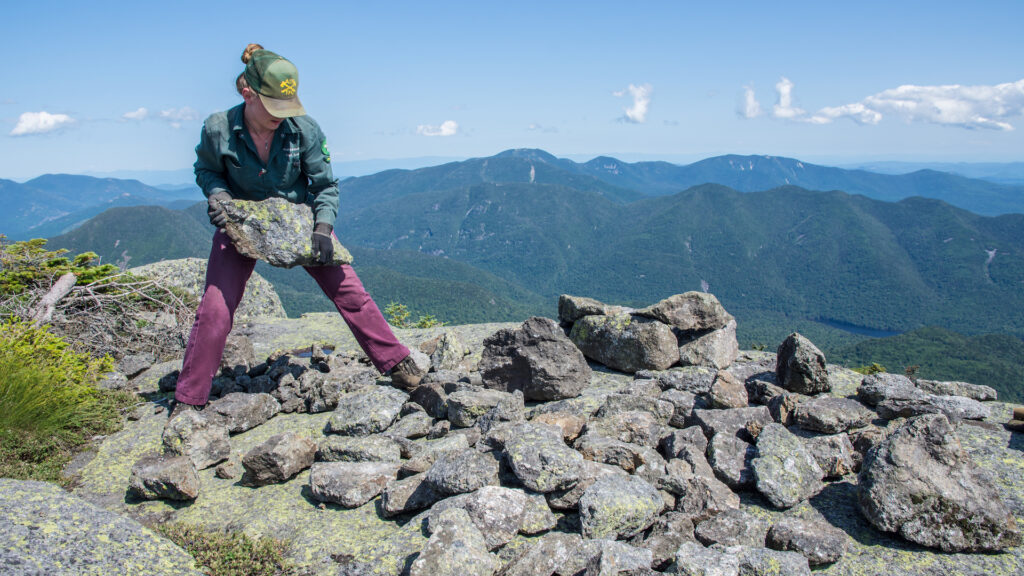 A person carrying a rock on a summit