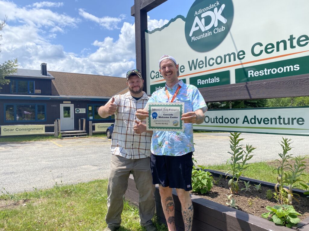 Two men standing in front of a sign while holding a certificate