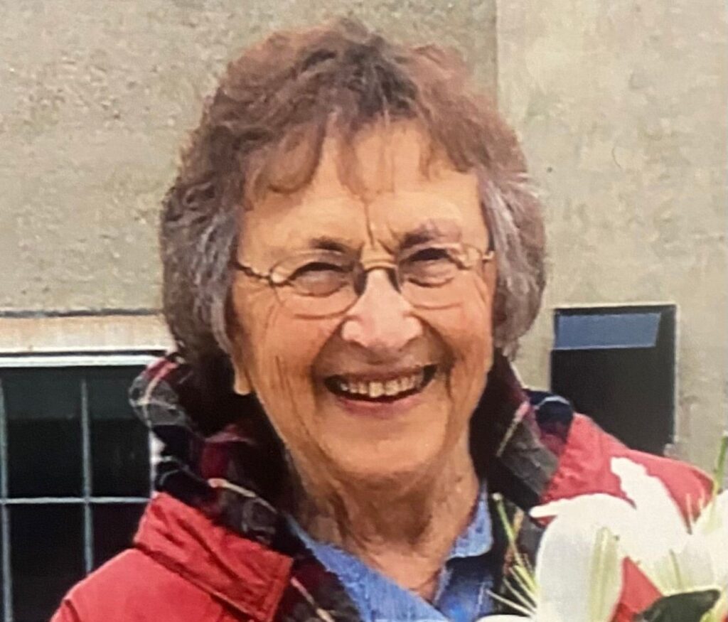 photo of a woman wearing glasses, smiling, and wearing a red coat