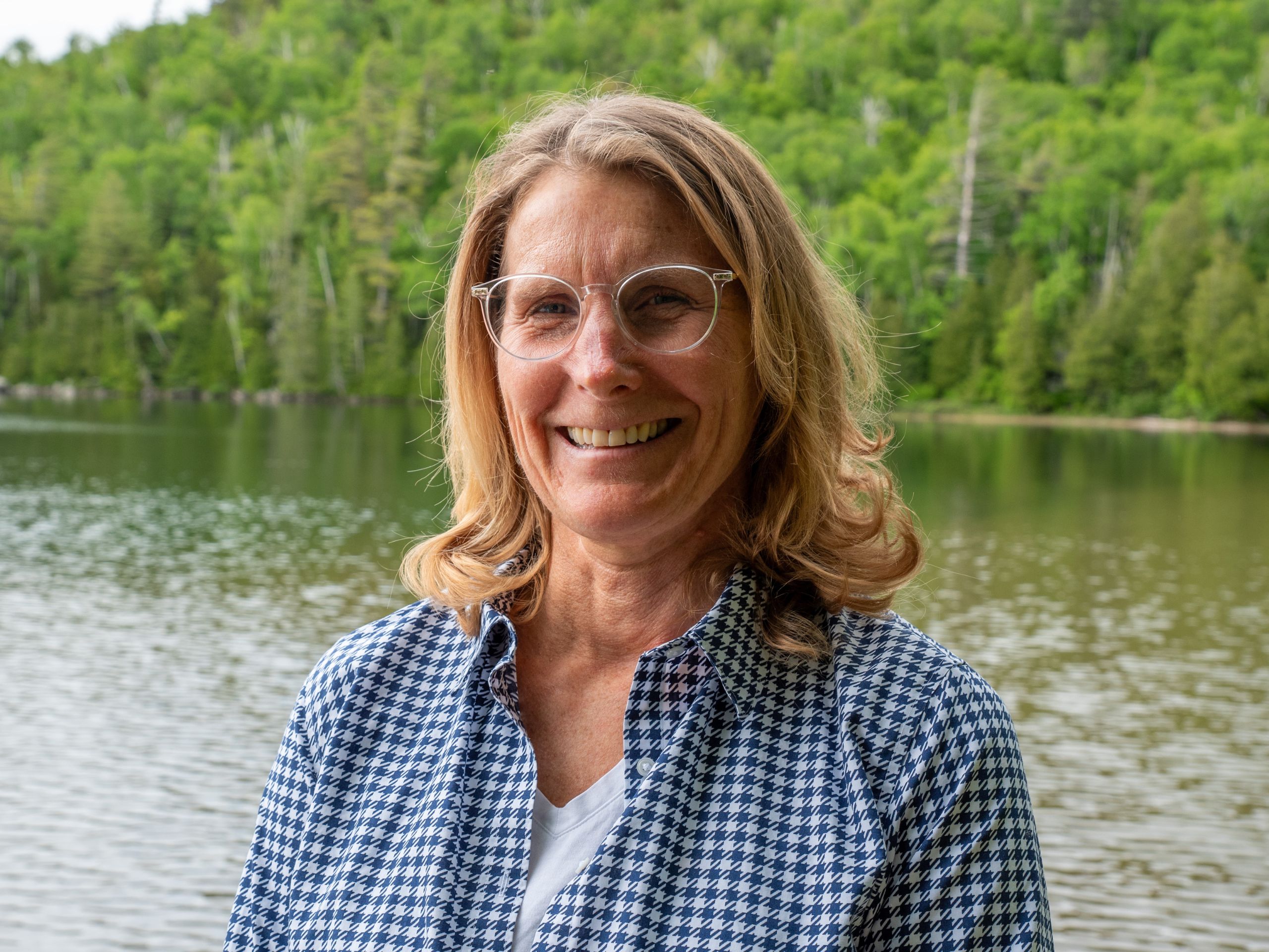 portrait of a woman standing in front of a lake with trees in the background