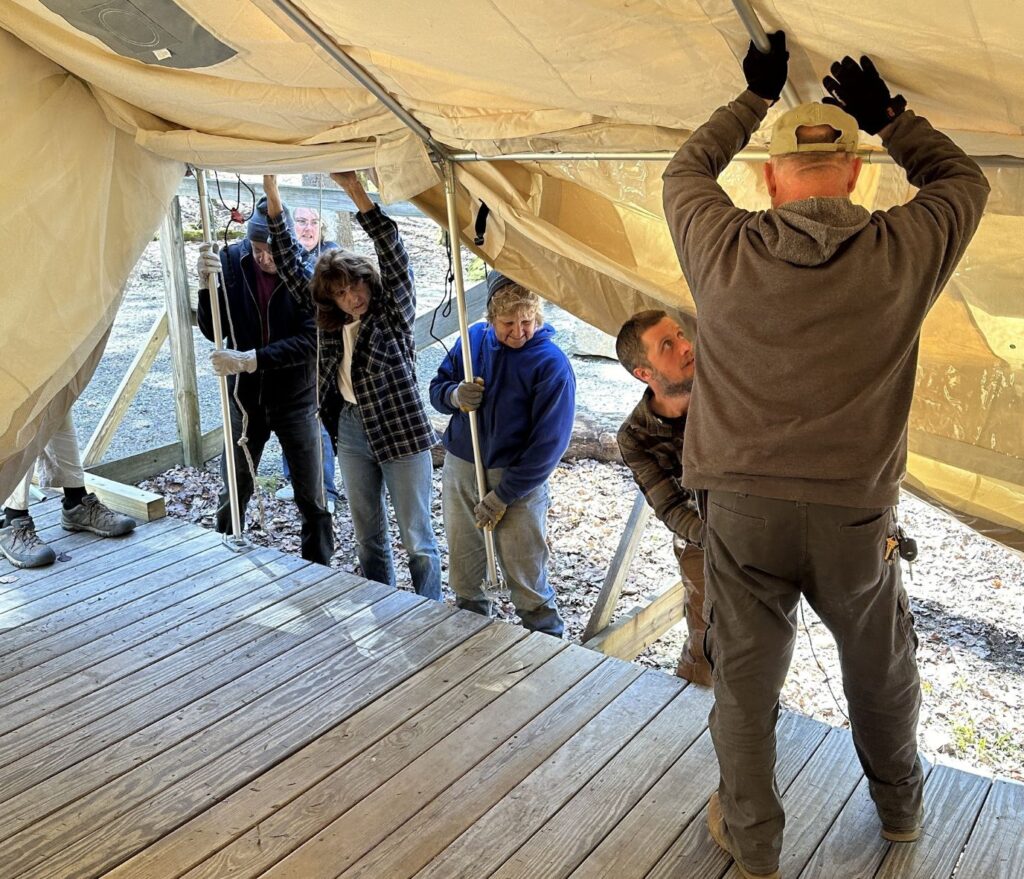volunteers setting up a canvas cabin on a wooden platform