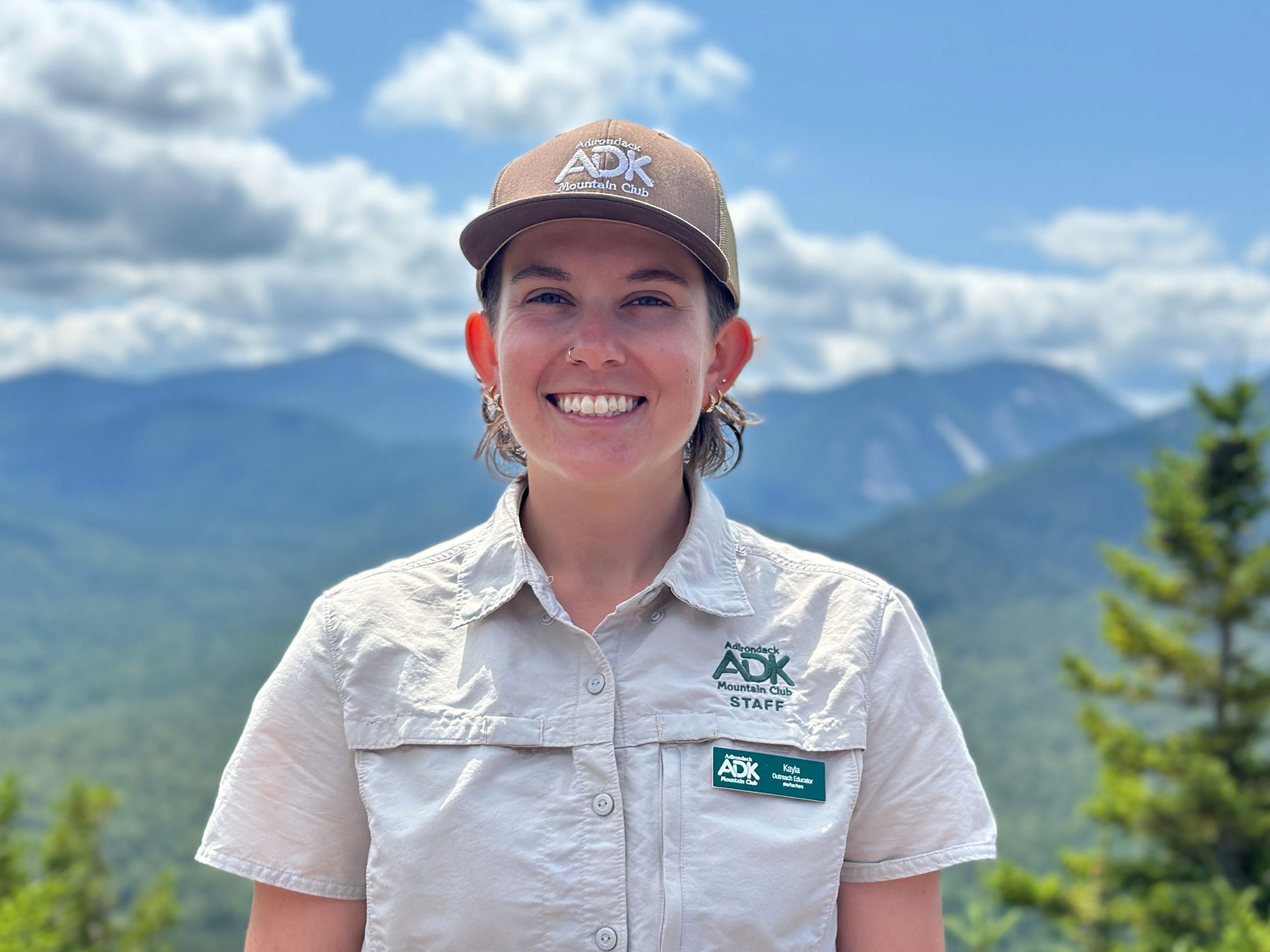 portrait photo of a woman wearing a hat with mountains in the background