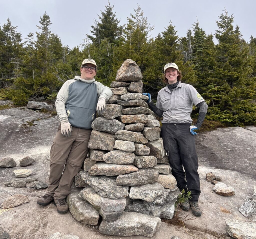 two summit stewards standing beside a large cairn