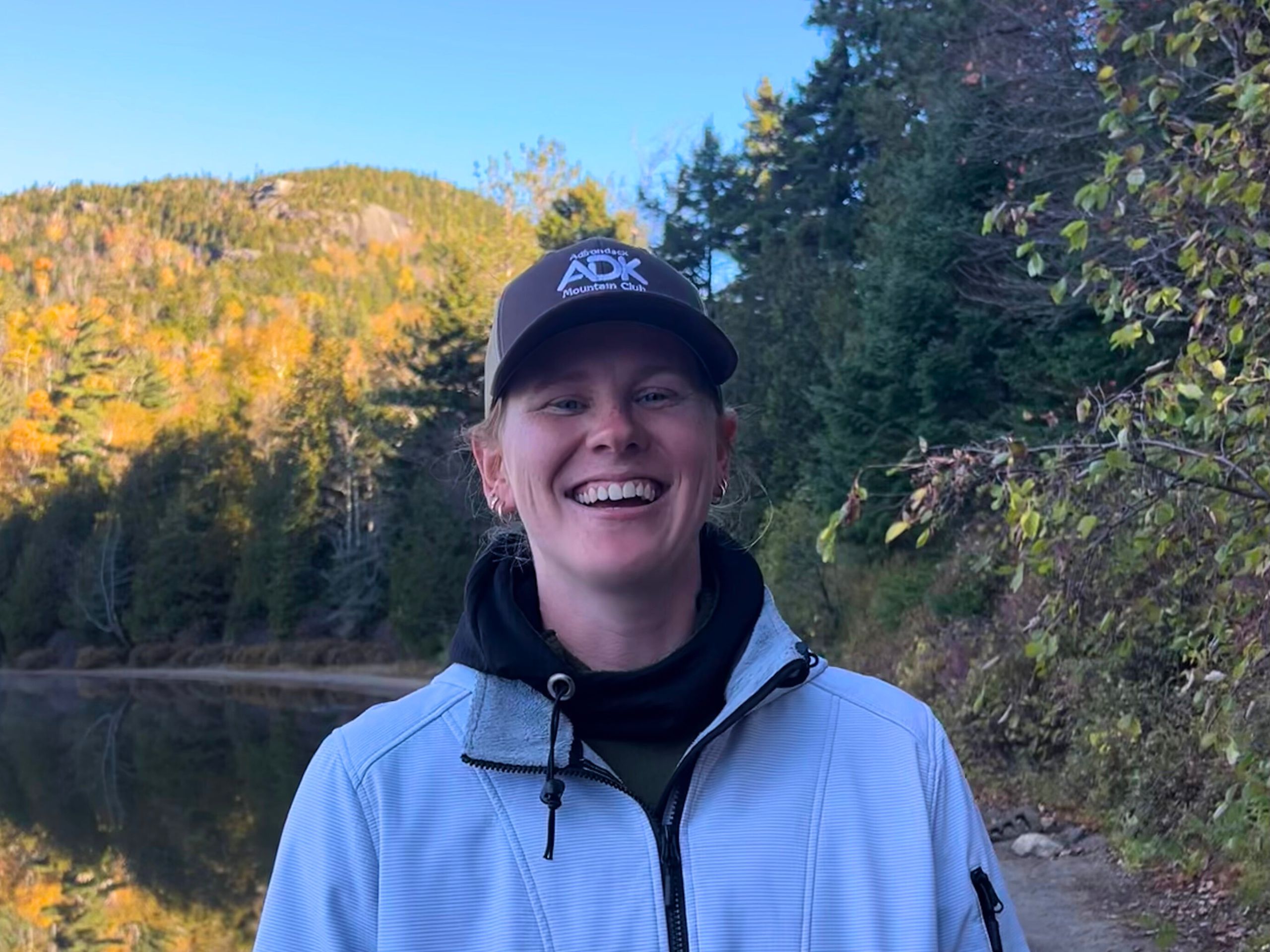 a woman wearing a hat and smiling by a lake
