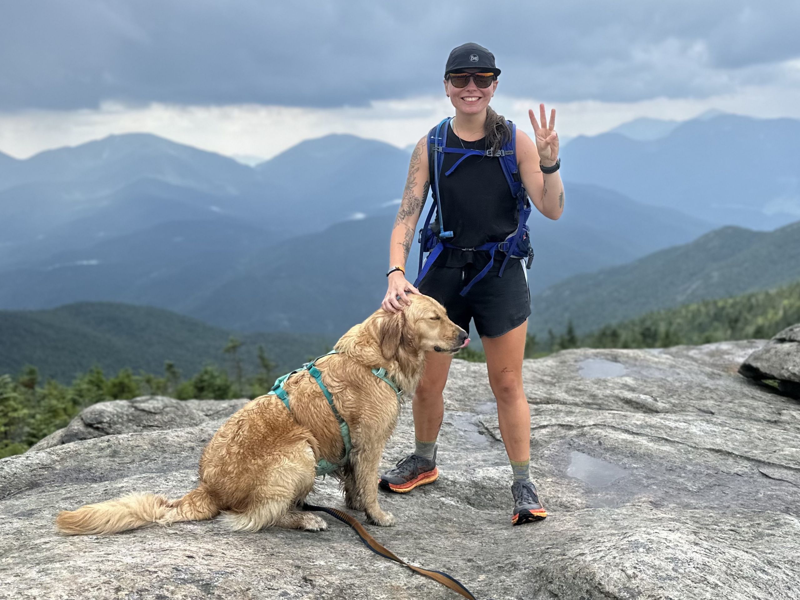 woman stands with dog on a mountain summit