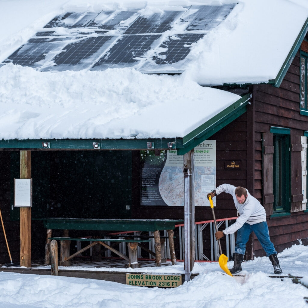 man shovels snow off the porch at Johns Brook lodge