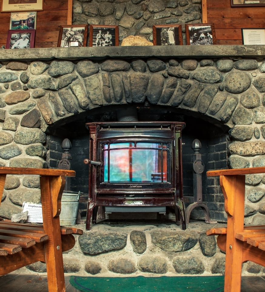 two chairs facing a wood stove in a stone fireplace