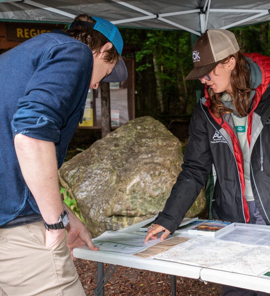 a trailhead steward speaking to a hiker while pointing at a map