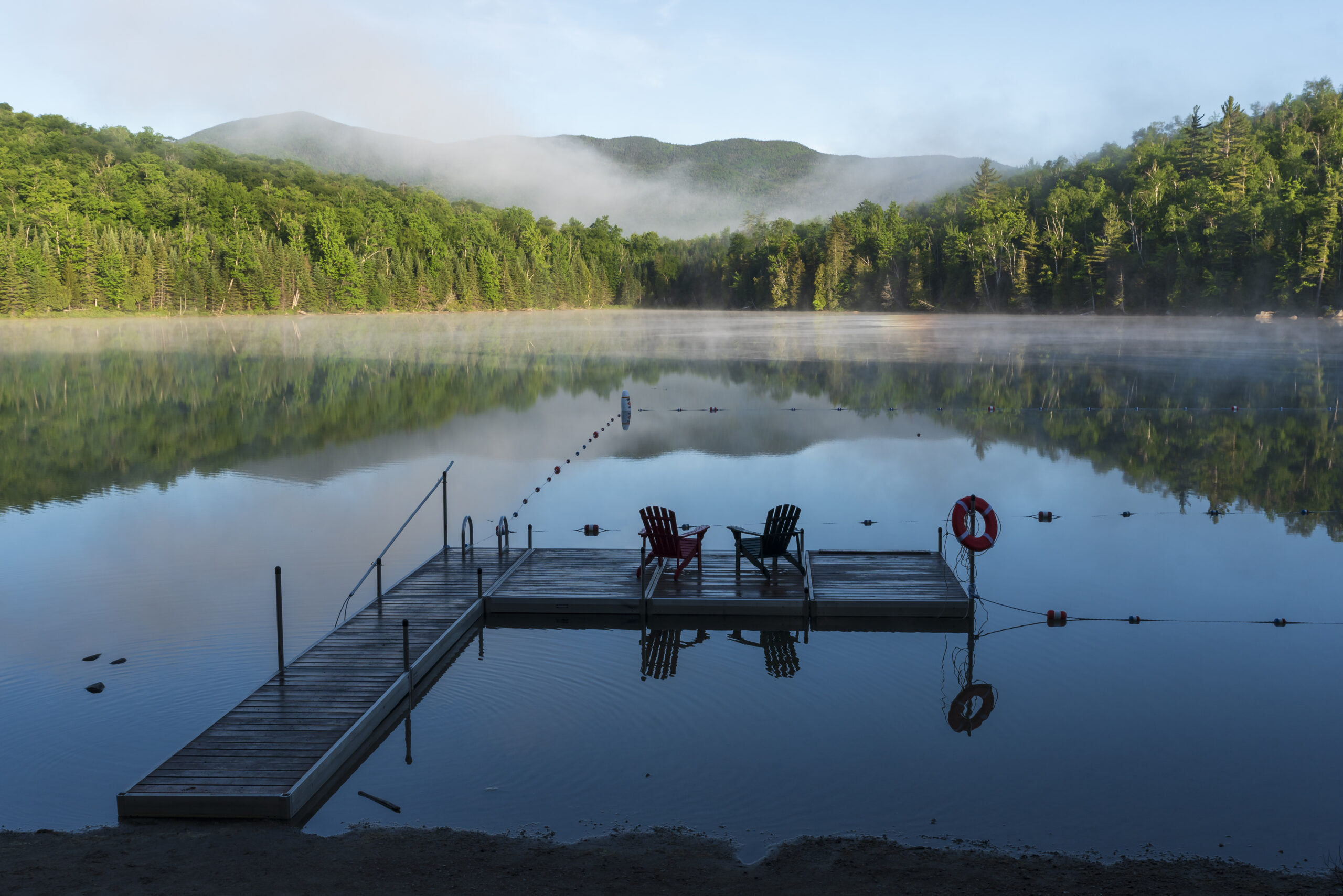A view of the dock with adirondack chairs on heart lake during the early morning