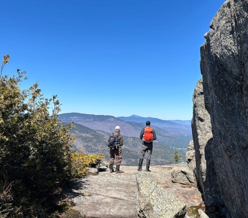 two hikers looking out on a mountain summit on a bluebird day
