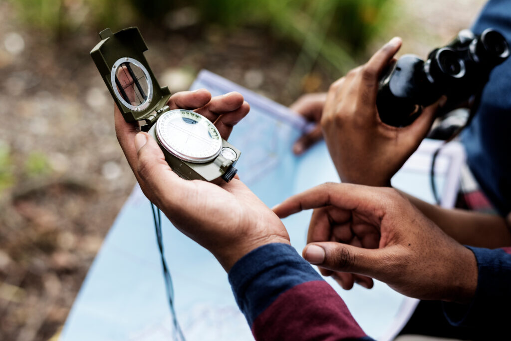 Couple looks at map with compass and binoculars in hand.