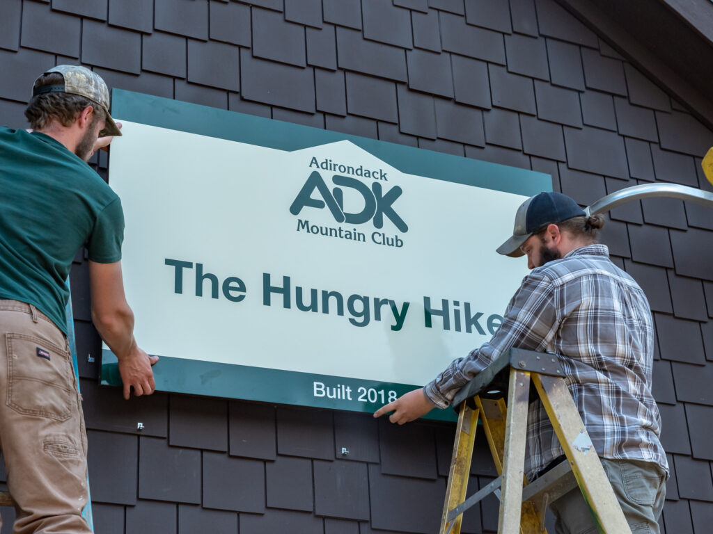 two men hanging a sign that reads "The Hungry Hiker"
