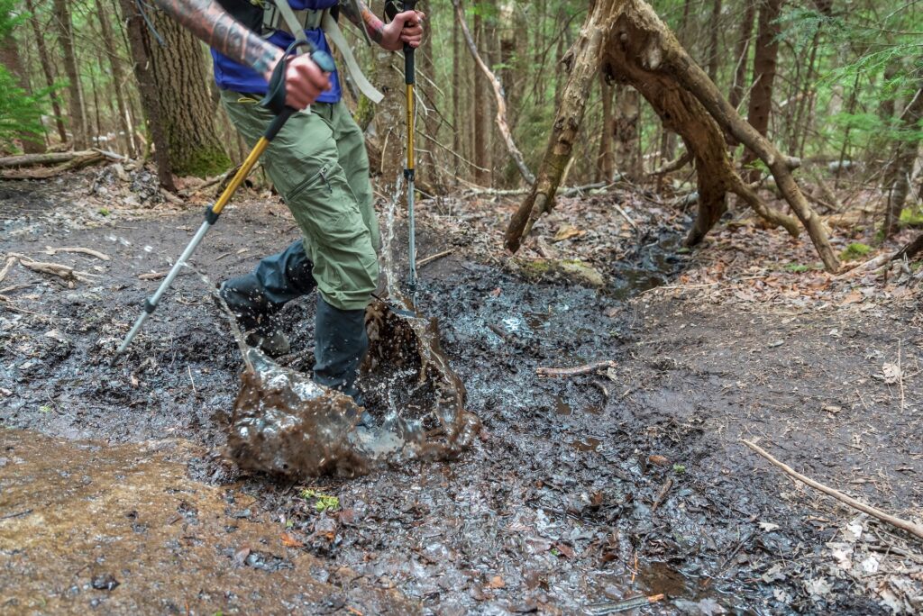 a hiker walks through a muddy section of trail in the adirondacks
