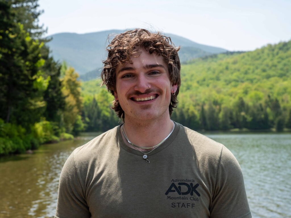 person with long curly hair stands in front of lake