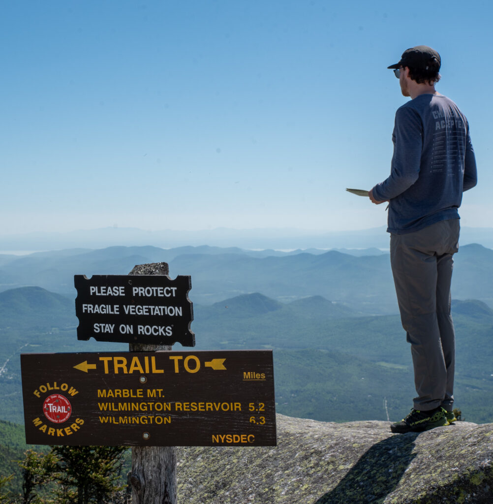 hiker stands on a rock at the summit of whiteface