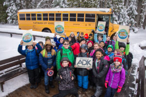 a group of students stand in front of a bus at adirondak loj front porch