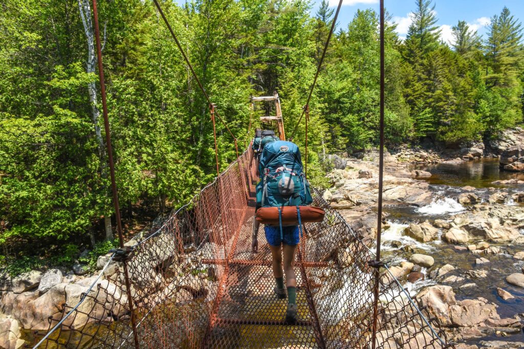 hiker crosses a bridge on a backpacking trip