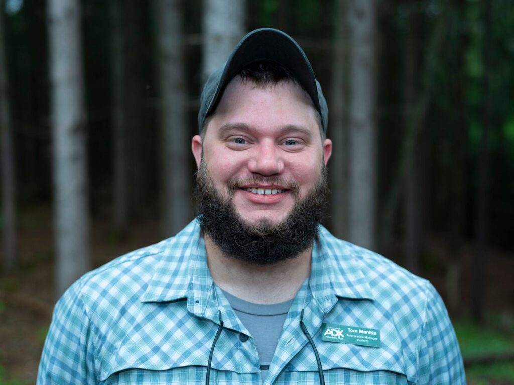 man with beard wearing a hat against wooded background