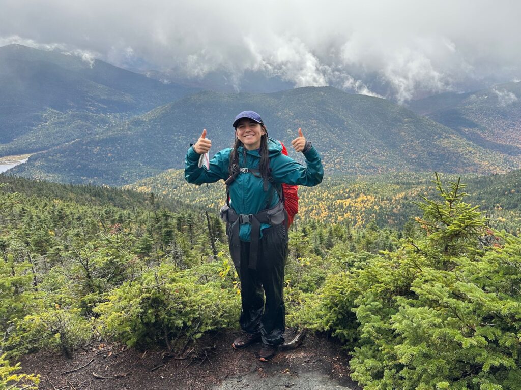 a woman in a hat and rain jacket near a mountain summit on a rainy day