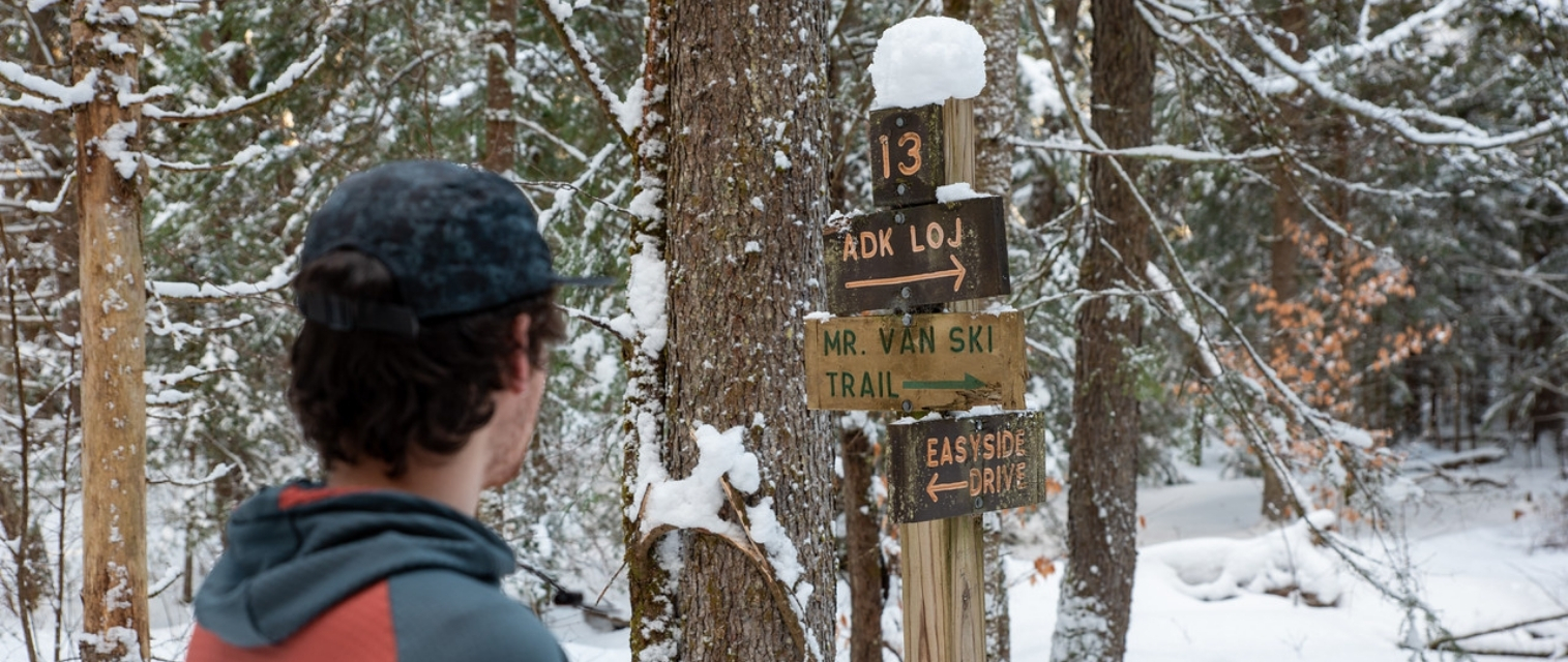 man wearing a hat looks a signpost on the trail in winter
