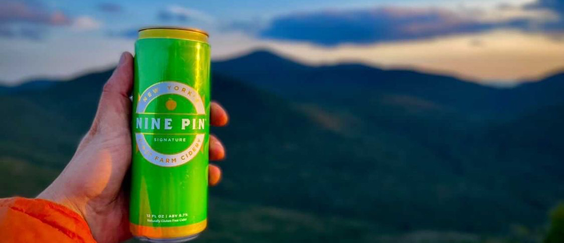 hiker holding nine pin cider can at mountain summit
