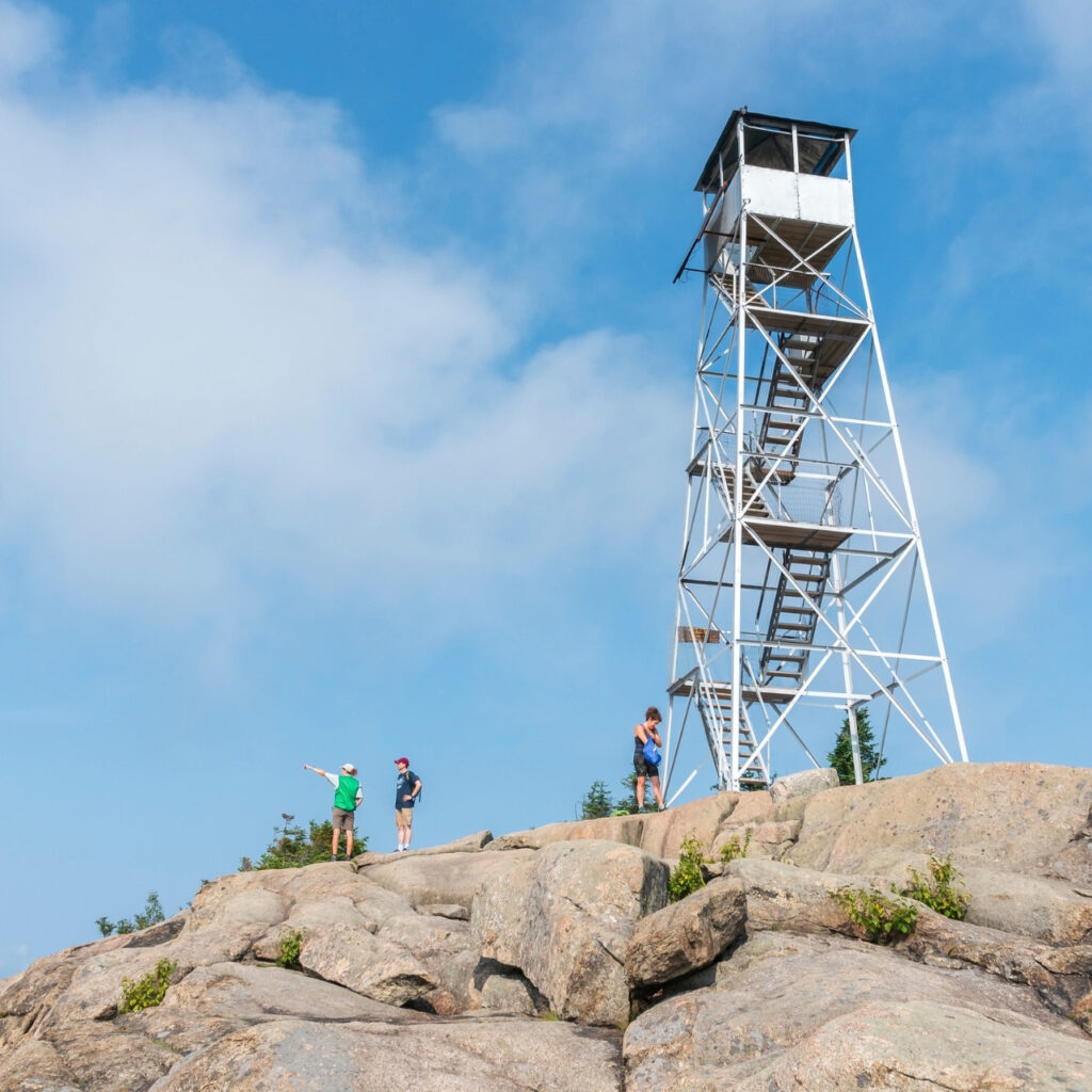 a summit steward speaks to a hiker next to a fire tower in the adirondacks