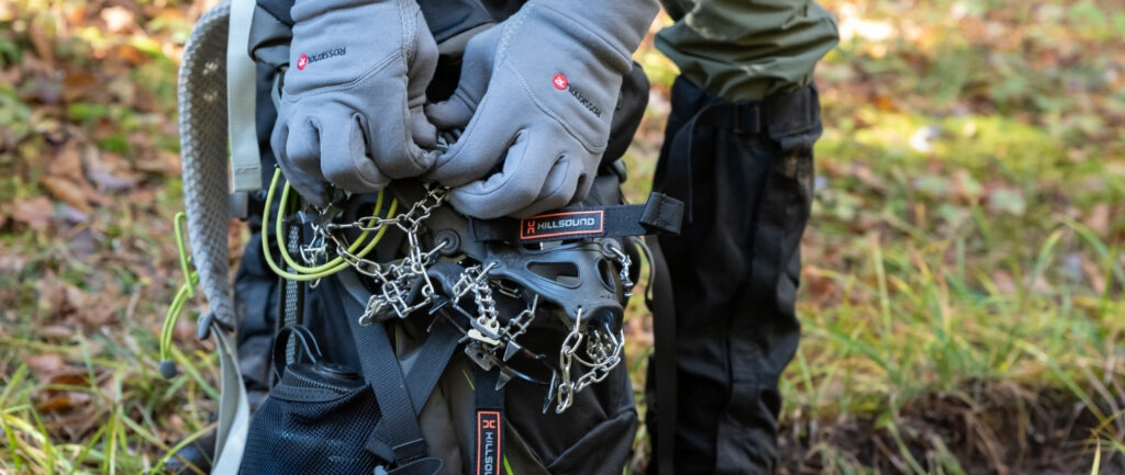 person wearing gloves adjusts microspikes on backpack