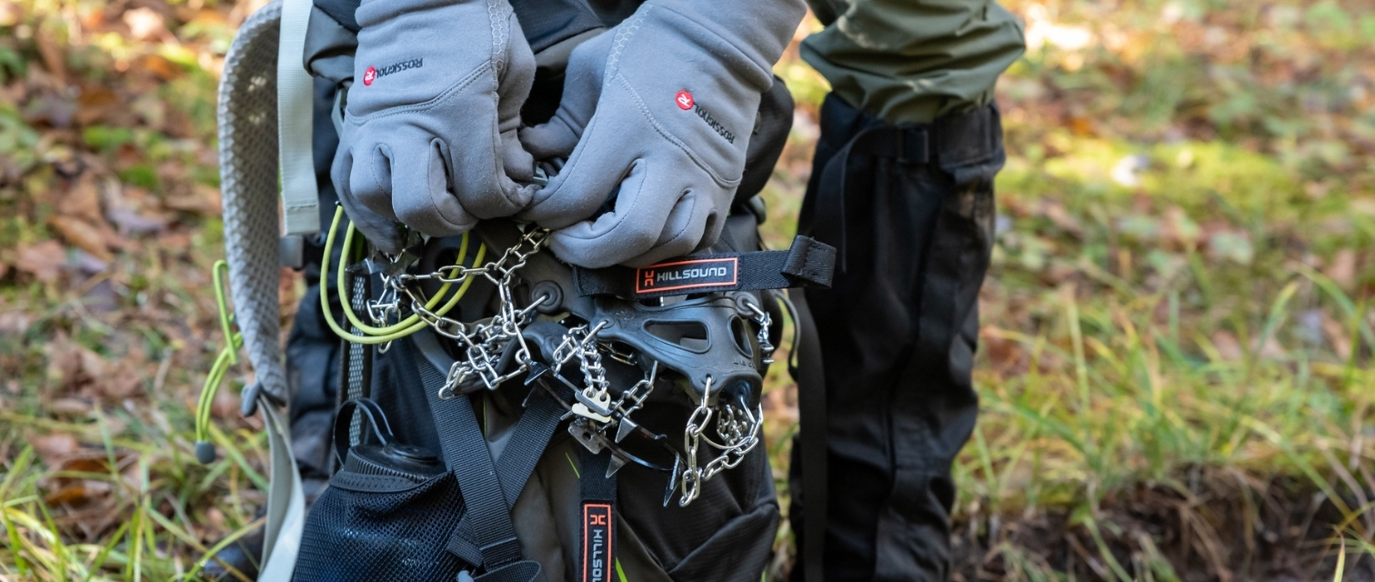 person wearing gloves adjusts microspikes on backpack