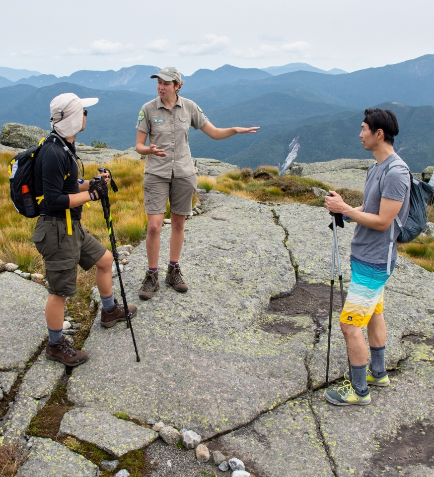 summit steward standing with and speaking to two hikers