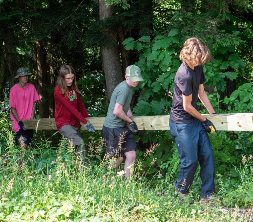teens carry wood for bridging through the woods