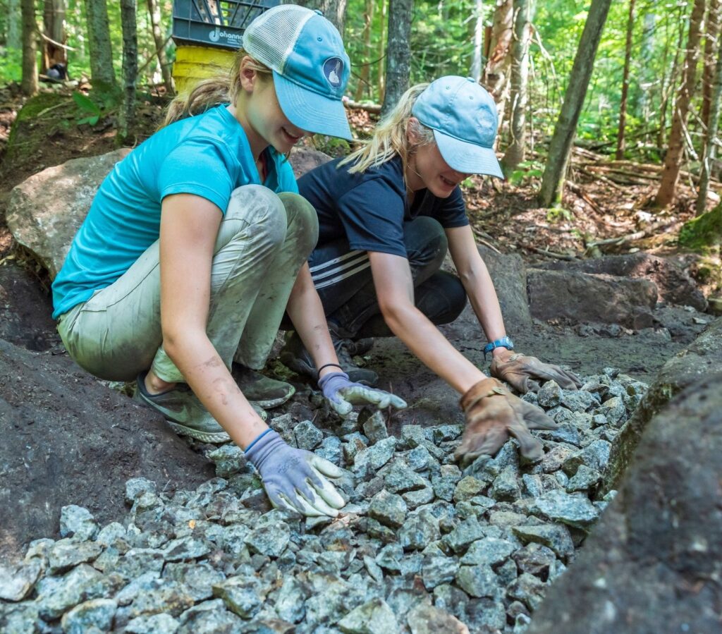 teens wearing hats lay rock at volunteer trail project