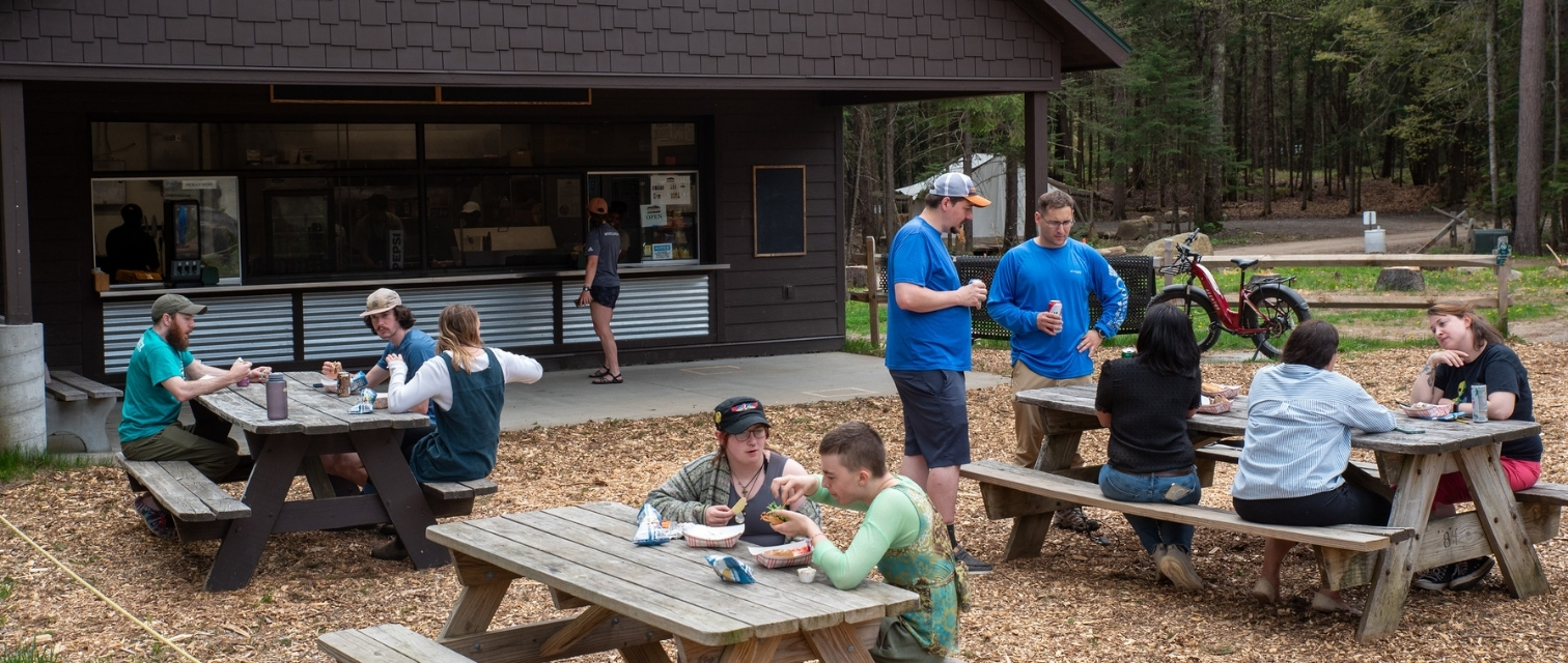 a group of people eating at picnic tables in front of a food stand