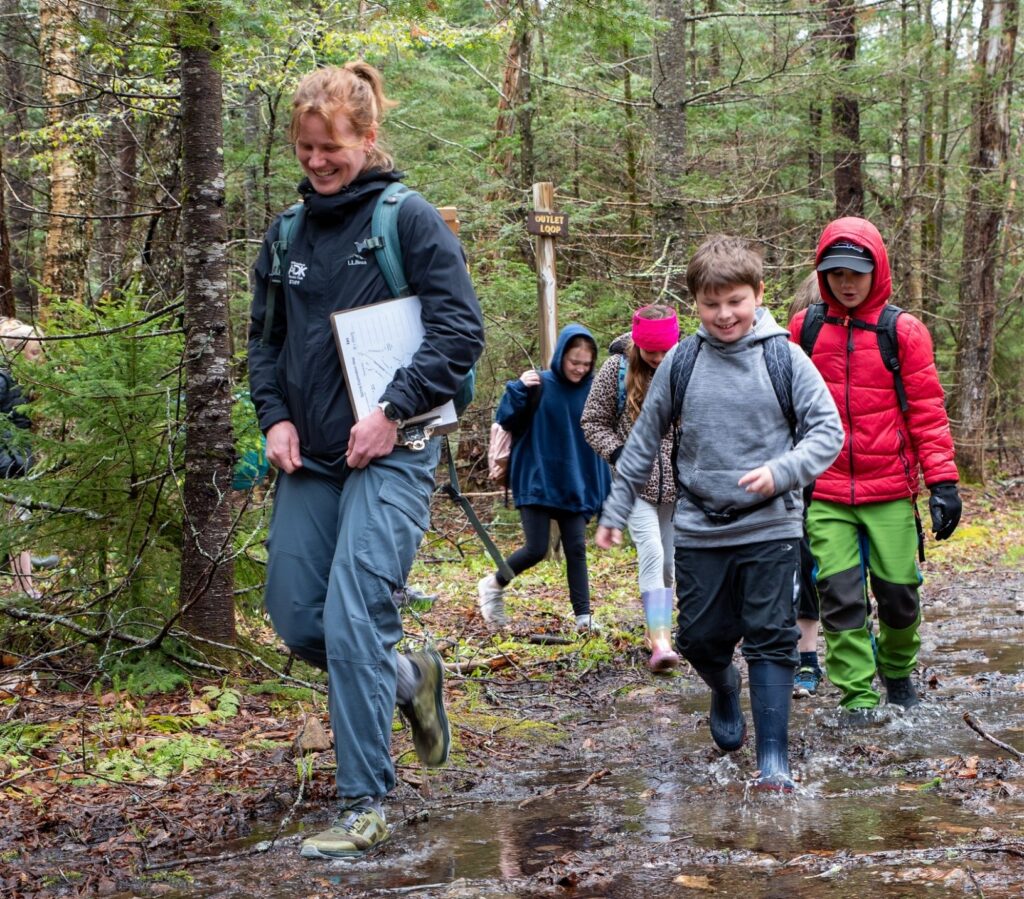 a teacher and group of students walk through a wet and muddy trail