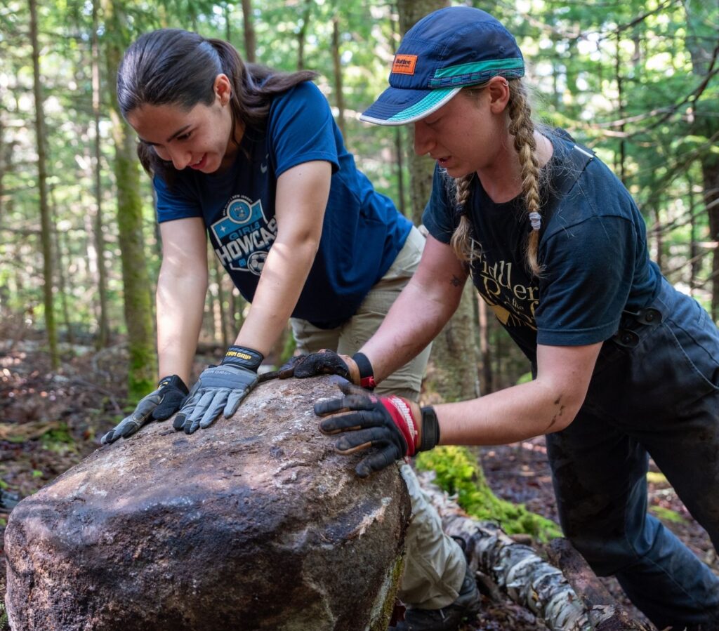 two women push a rock in the woods