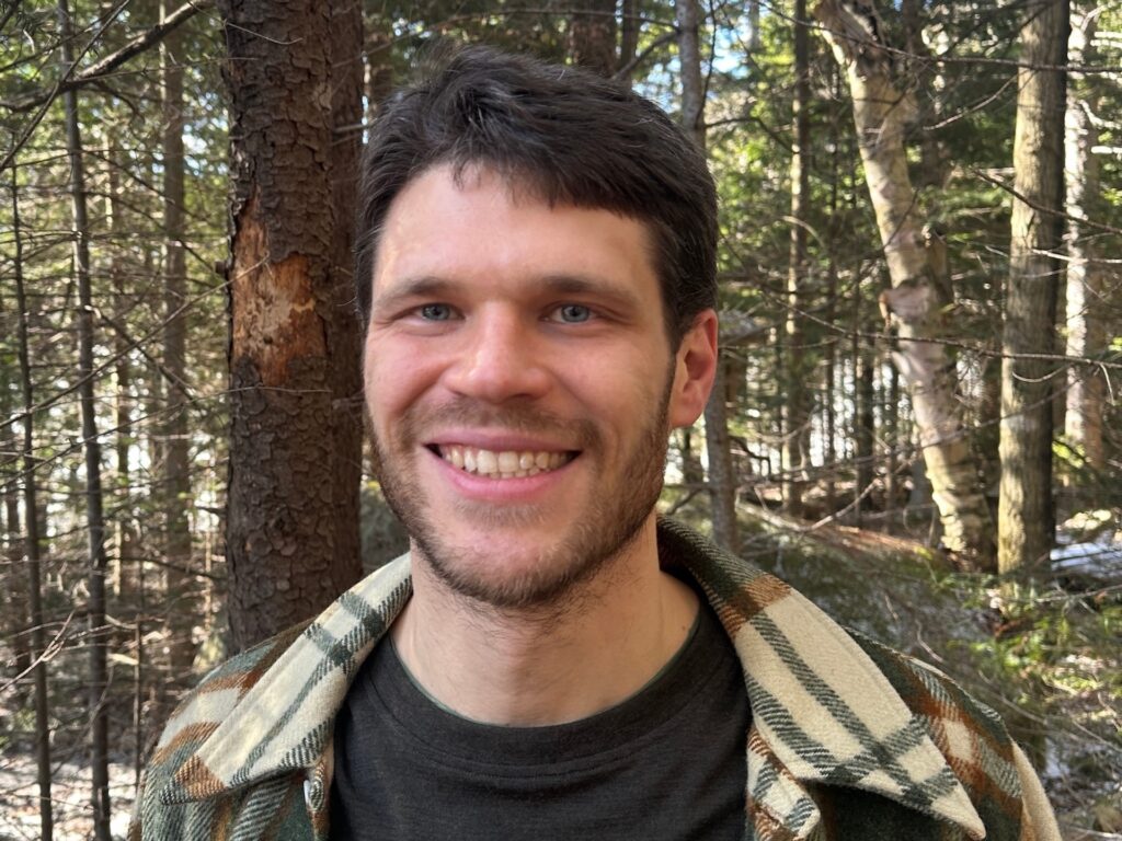 portrait photo of a dark haired man with a wooded background