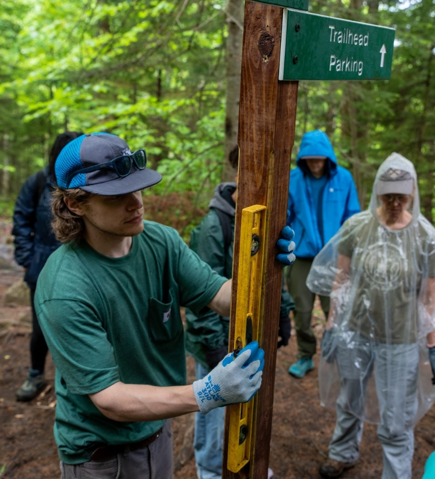 man wearing a hat uses a level on a wayfinding sign post