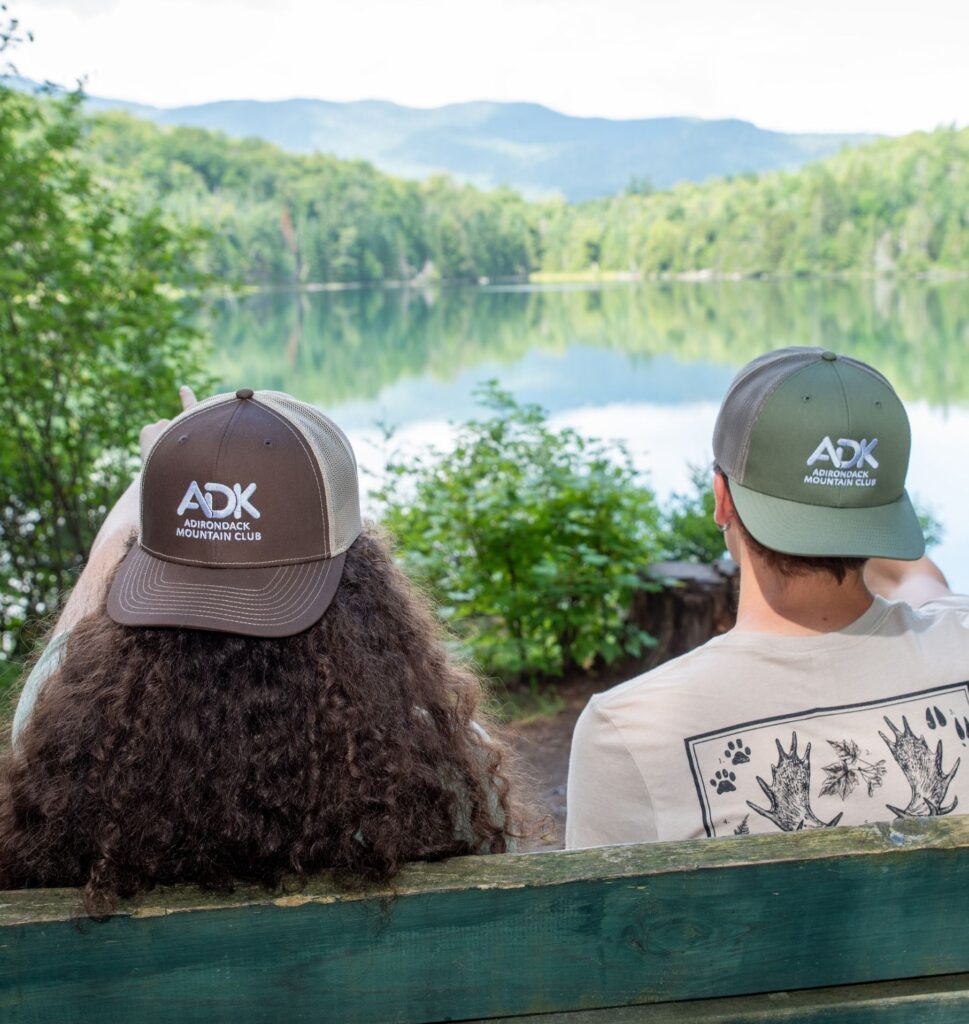 two people sitting on a bench by Heart Lake wearing backwards ADK trucker hats