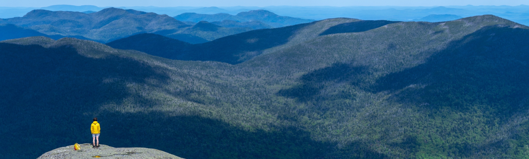 a hiker wearing a yellow jacket stands at the summit of wright peak