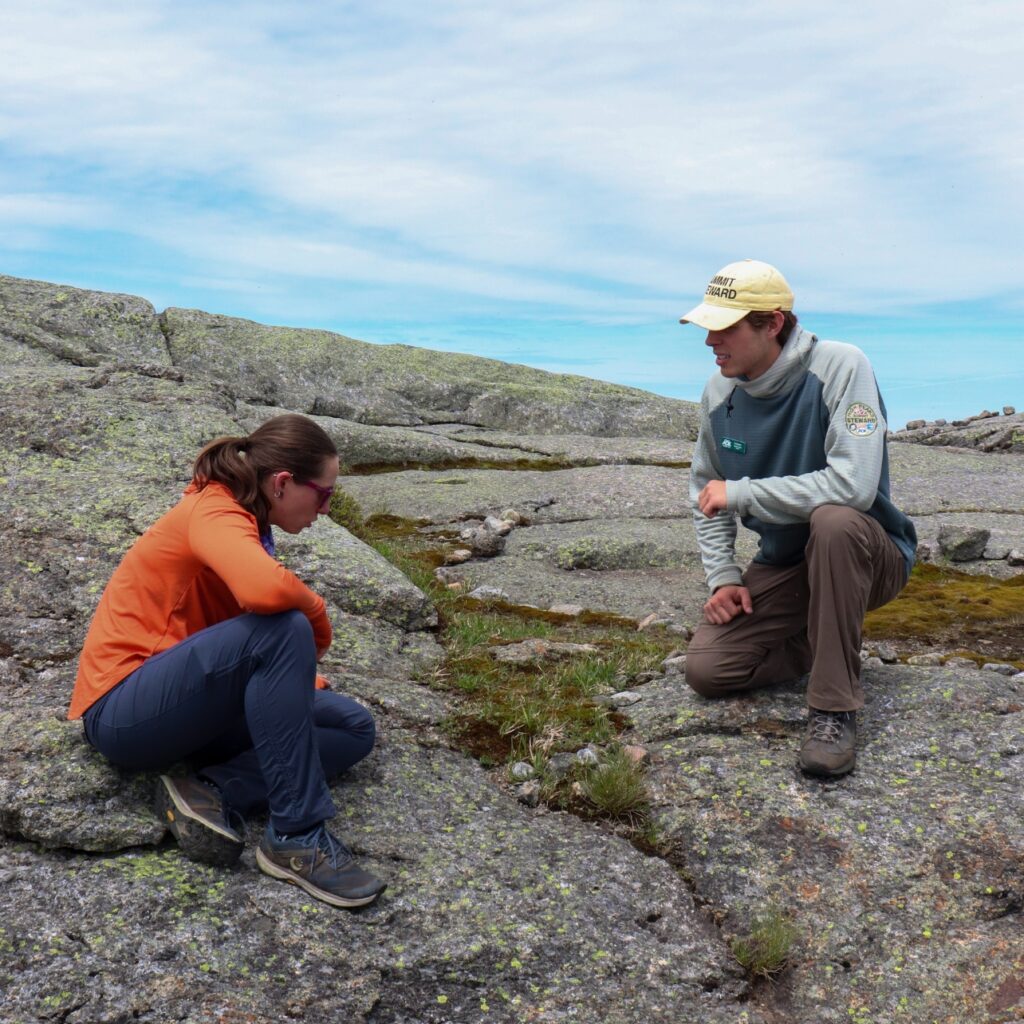 a summit steward kneeling and speaking to a hiker on an Adirondack summit